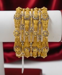 Set of gold bangles with intricate designs on a red satin background