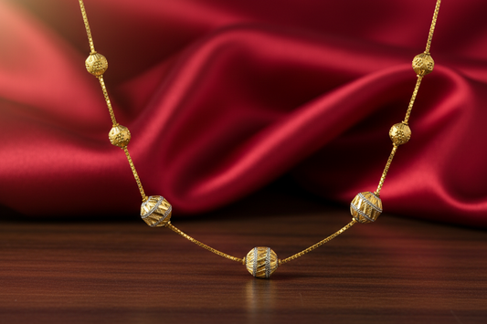 Gold necklace with spherical beads on a red fabric background